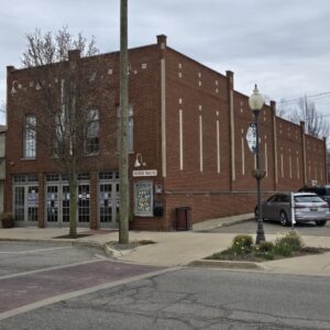 A brick building labeled "Vickers Theatre" stands on a street corner with parked cars and a cloudy sky above.