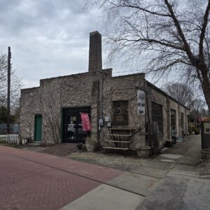 Brick industrial building with a tall chimney, front entrance, and a red OPEN sign on a cloudy day.